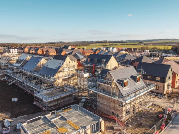 UK residential construction site with site workers in hi-viz PPE alongside a JCB backhoe outside newly-built brick houses.
